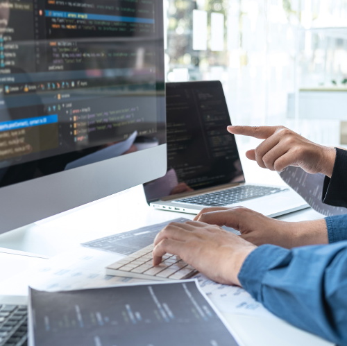 tech Manos sobre el teclado de un ordenador de sobremesa, y una mano de una persona diferente apuntando con el dedo a su pantalla